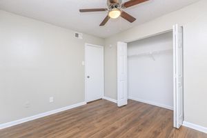 An empty room featuring light gray walls and wood-style flooring. A ceiling fan hangs from the ceiling, and a closet with white sliding doors is visible on the right side. The space is well-lit, providing a clean and modern appearance suitable for various uses.