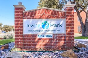Brick sign for Irving Park, featuring the logo and address "1812-1826" along with the website and phone number. Surrounding the sign are decorative stones and landscaping elements.