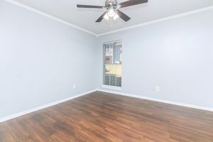 Empty room with light gray walls and hardwood flooring. A ceiling fan with lights is mounted in the center. There is a window with horizontal blinds on the right side, allowing natural light to enter. The room has a simple, clean appearance, suitable for various purposes.