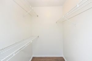 Empty closet with white wire shelving along the walls. The walls and ceiling are painted white, and the floor is wooden. The space is well-lit and uncluttered, providing a blank canvas for organization or storage.