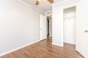 A well-lit room with light gray walls and hardwood flooring. Two doors are visible: one leading to a closet and the other to an adjoining space. A ceiling fan is mounted above, and the room appears clean and organized, with no furniture present.