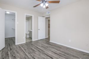 A spacious, well-lit room with wood-look flooring, a ceiling fan, and a light-colored wall. Doors leading to a closet and a bathroom are visible. The overall ambiance is clean and inviting, suitable for a bedroom or living space.