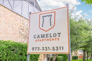 Sign for Camelot Apartments featuring a castle logo, surrounded by greenery and clear blue skies. The text includes "Camelot Apartments" and the phone number "972-231-5311."