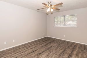 A spacious, empty room with light gray walls and a ceiling fan. The floor features wood-like laminate, and there is a window with blinds allowing natural light. The overall atmosphere is bright and airy, ideal for decorating or furnishing.