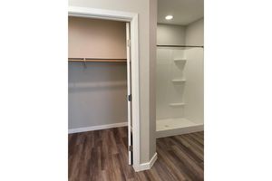 A view of an interior space featuring an open bathroom area with a modern shower and a separate closet. The shower has built-in shelves, and the flooring is made of wood-like planks. The walls are painted in neutral tones, creating a clean and spacious look.