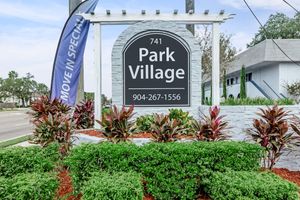 A sign for "Park Village" located at 741, featuring a phone number (904-267-1556) and surrounded by decorative plants and landscaping. A banner reading "Move In Special" is visible to the left, indicating an attraction or promotion.
