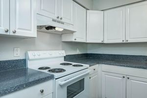 A clean, modern kitchen featuring white cabinetry, a gray countertop, and a white stove with four burners and an oven. The space has a minimalist design with well-organized storage and natural light, creating a bright and inviting atmosphere.