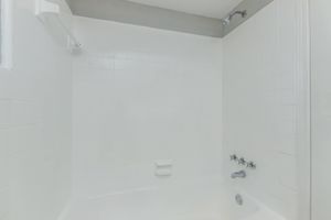 A clean, empty bathroom with a white tiled shower and bathtub. The walls are also white, with minimal fixtures visible including a showerhead and faucet controls. The overall look is bright and spacious, conveying a sense of simplicity and freshness.