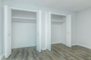 Two open closet doors in a room with light gray walls and wooden flooring. The closets have shelves inside, and the space is well-lit and minimalistic, conveying a clean and organized atmosphere.