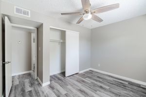Spacious modern bedroom with ceiling fan, closet, grey wood flooring, and doorway