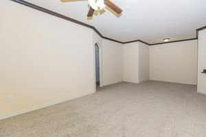 A spacious, empty living room with beige walls and light carpet. The room features a ceiling fan and a wide archway leading to another area. There is a single light fixture on the ceiling, creating a bright atmosphere. The space is ready for furnishing and personalization.
