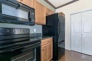 A modern kitchen featuring black appliances, including a microwave, oven, and refrigerator, set against wooden cabinetry and dark granite countertops. The walls are painted a soft green, and there is a closed double-door closet visible in the background.