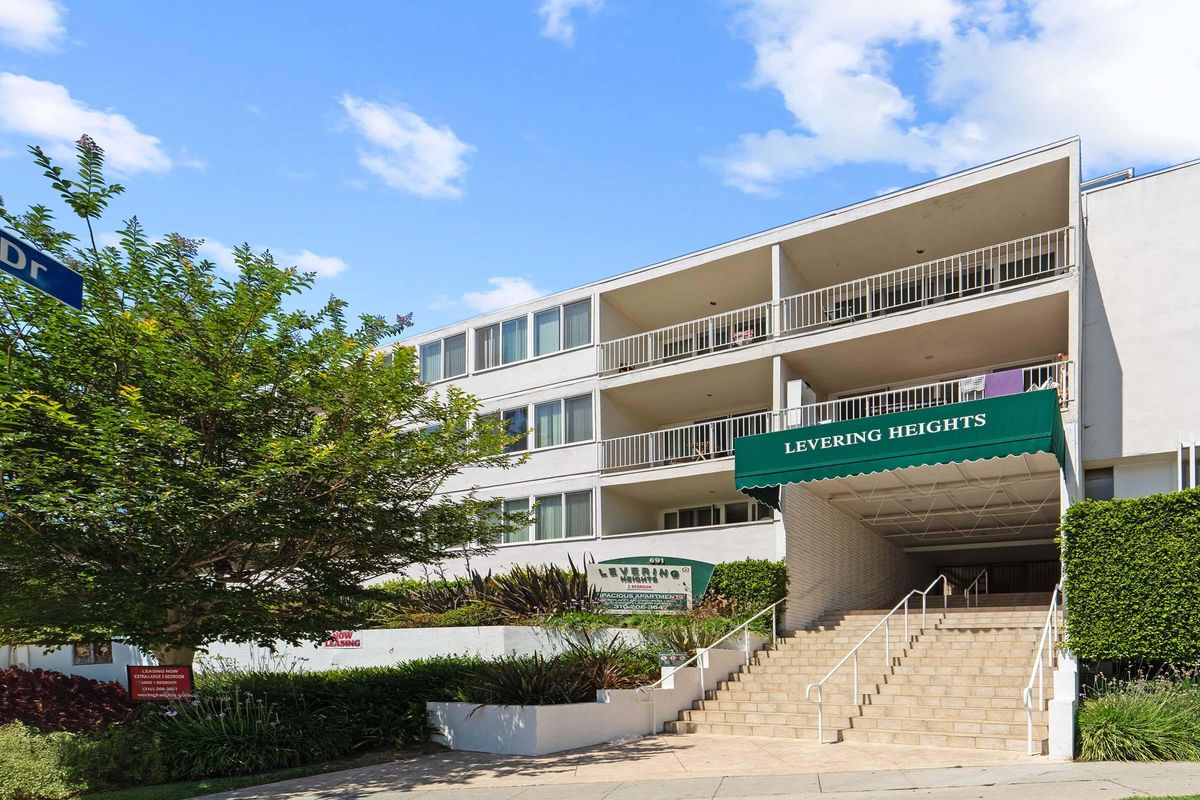 A multi-story residential building with a green awning labeled "Levering Heights," featuring balconies and a series of steps leading up to the entrance. Lush landscaping and blue skies are visible in the background.