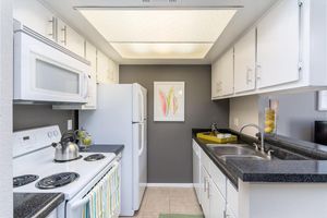 Walk through kitchen with white cabinets, white appliances, and dark grey counter tops