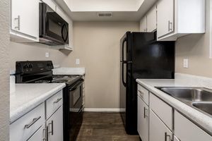 Galley way kitchen with white cabinets, black appliances, and a small window over the sink