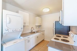 Stacked white washer and drier next to a renovated kitchen with white cabinets