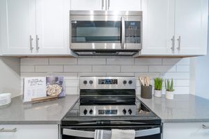 Close up of stainless steel stove top and microwave next to grey granite countertops