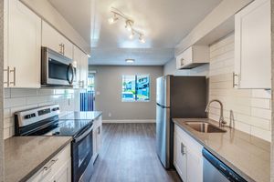 Galley way renovated kitchen with white cabinets, stainless steel appliances, and white back splash