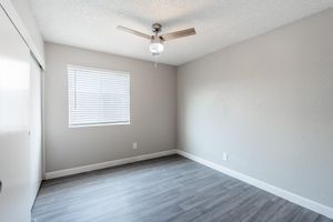Open modern bedroom with wood floors, ceiling fan, and window