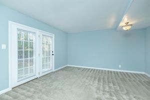 A spacious room featuring light blue walls and soft carpet flooring. The room includes a set of double doors with glass panels leading to an outdoor area, and a light fixture is mounted on the ceiling, providing a bright and airy atmosphere.