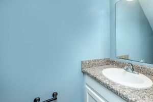 A clean, modern bathroom with a light blue wall and a granite countertop. There's a round sink with a chrome faucet, and a mirror reflects the space. A black toilet paper holder is mounted on the wall, adding to the minimalist design. Soft lighting enhances the fresh and airy atmosphere.