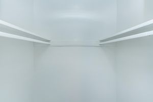 A view of an empty closet with plain white walls and two horizontal shelves. The space appears clean and minimalistic, lacking any stored items or clutter. The lighting is bright, enhancing the simplicity of the interior.