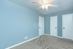 A light blue room featuring two closed doors, a ceiling fan with lights, and beige carpet. The walls are freshly painted, and there is empty space, suggesting a clean and minimalist design suitable for various uses.