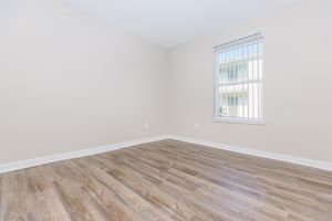 Bright, empty room featuring light-colored walls and a wood laminate floor. A single window with vertical blinds allows natural light to enter, creating a spacious and inviting atmosphere. The room is ready for furniture and personal touches.