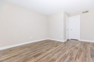 A vacant room with light beige walls and a wooden floor. Two white doors are visible on the right side, leading to separate spaces. The room has an open and airy feel with ample natural light, though no furniture or decor is present.