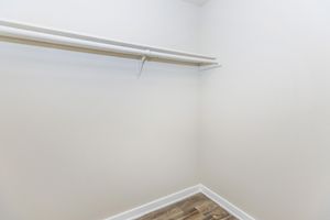 Empty closet with a white wall and a single hanging rod. The floor is made of light-colored wood, creating a clean and minimalistic look.