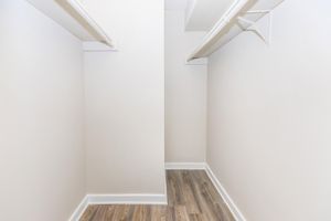 A bright, uncluttered walk-in closet featuring two parallel walls with white shelves and a light-colored floor. The walls are painted in a soft neutral tone, creating an open and spacious feel. The closet is empty, showcasing ample room for storage or organization.