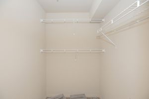 A spacious, empty closet featuring white wire shelving. The walls are painted a light color, and there’s a small section of the floor visible with some gray wooden planks. The closet appears clean and organized, with ample storage space visible in the design.