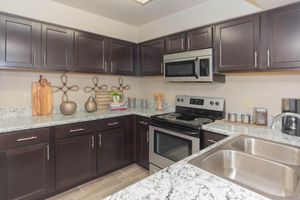 Modern kitchen featuring dark wood cabinets, a stainless steel microwave and oven, a granite countertop with a double sink, and decorative items like vases and wooden cutting boards. The space is well-organized and bright, highlighting a contemporary design.