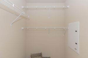 A well-organized, empty closet featuring two white wire shelves mounted on beige walls. A small wall panel is visible on the right side, and a woven basket sits on the floor, providing a tidy appearance. Ideal for storage and organization.