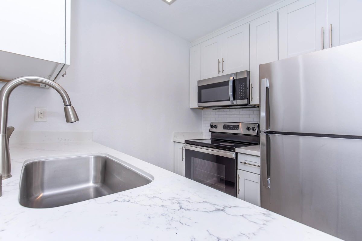 Modern kitchen interior featuring a stainless steel refrigerator, microwave, and stove. The countertop is made of white marble, and there is a sleek, modern sink. The cabinets are white with clean lines, creating a bright and contemporary atmosphere.