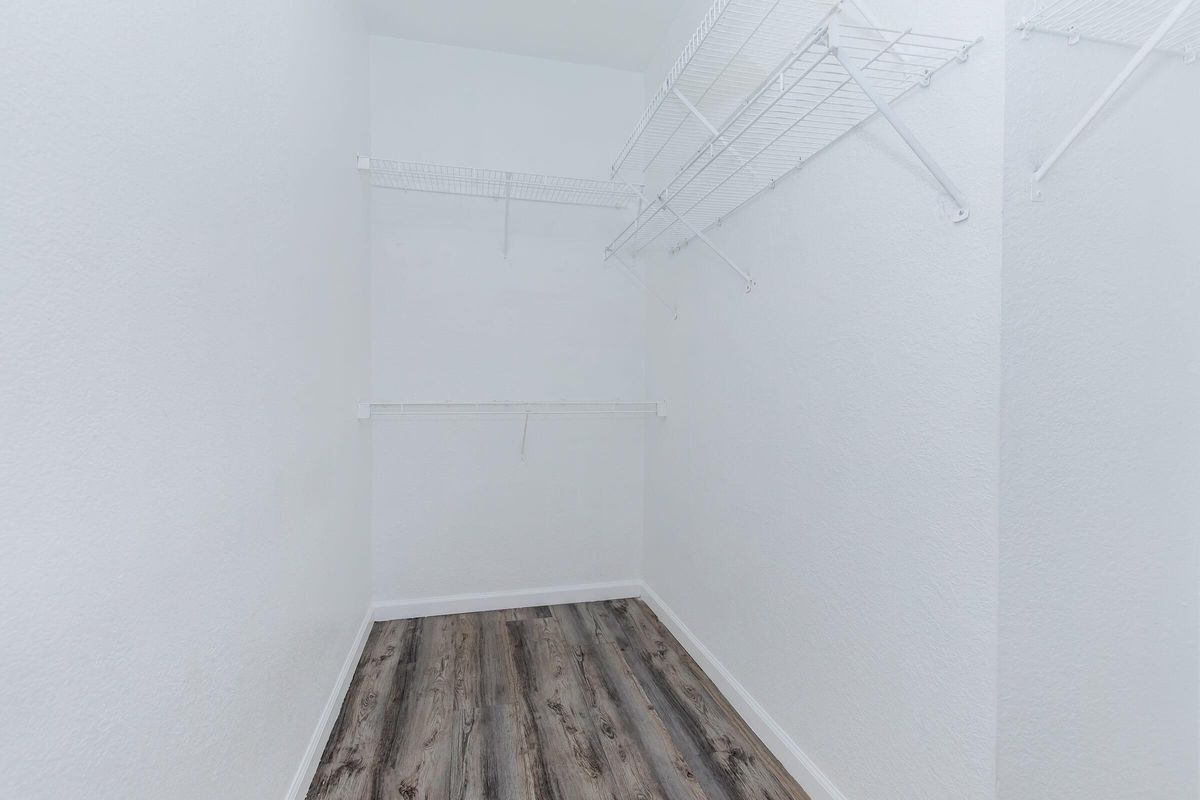A minimalist empty closet with white walls, wooden flooring, and wire shelving on two sides, creating an organized and spacious appearance.