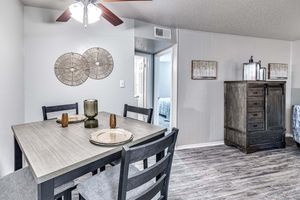 A modern dining area featuring a wooden table set for four with plates and a decorative candle holder. The walls are adorned with circular wall art, and the space includes a stylish cabinet and a ceiling fan. A doorway leads to another room, indicating an open-concept layout.