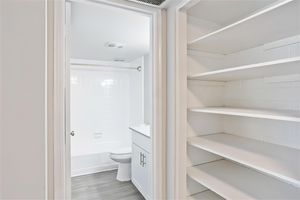 View of clean modern restroom from a walk in closet with floor to ceiling shelving