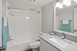 Modern bathroom with white tile shower, toilet, and grey quartz mirrored vanity