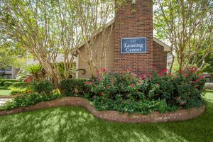 A well-maintained Leasing Center sign surrounded by lush greenery and colorful flower beds, set against a brick structure.