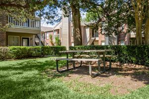 A picnic table situated on grass in a courtyard surrounded by shrubs and apartment buildings.