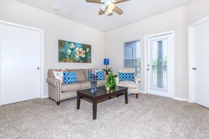Sofa, armchair and coffee table in carpeted living room with door to private balcony