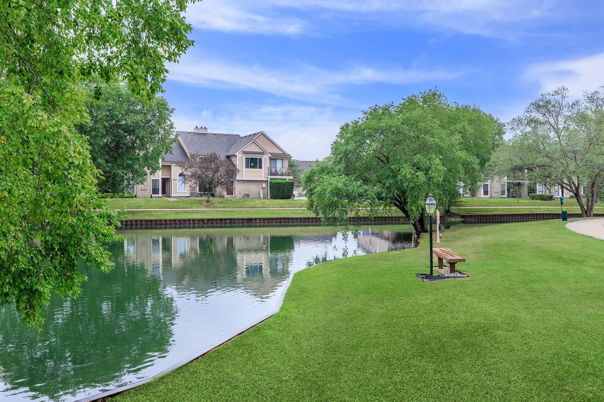 a body of water with green grass in front of a house
