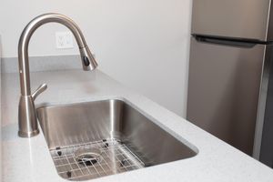 Close up of a stainless steel sink and faucet built into a grey quartz island